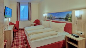 A hotel room with a bed, a desk, a chair, a TV, and a painting of a landscape. - Hotel Elbparadies (Pirna)
