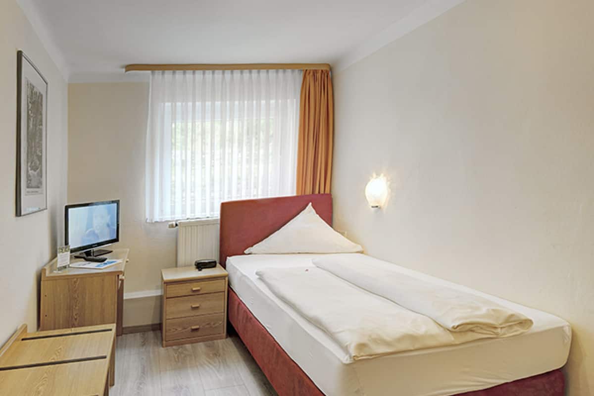 A bedroom with a bed, a desk, a chair, a television, and a window with curtains.