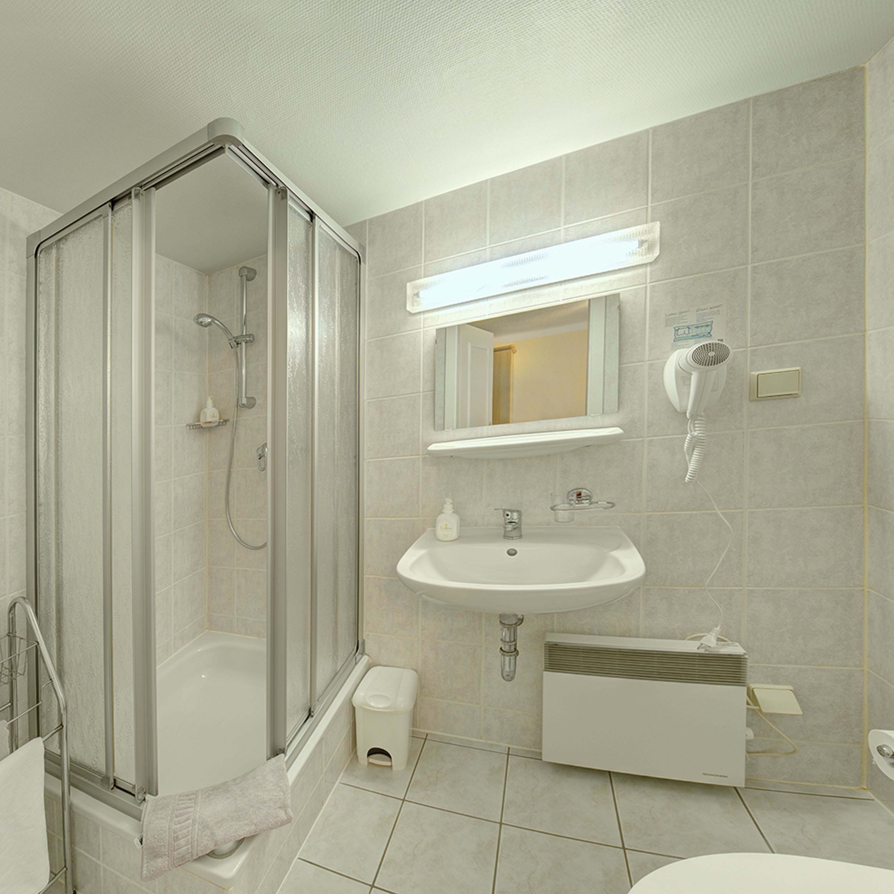 A modern bathroom with a glass-enclosed shower, a sink, a mirror, and a hairdryer.