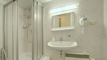 A modern bathroom with a glass-enclosed shower, a sink, a mirror, and a hairdryer.
