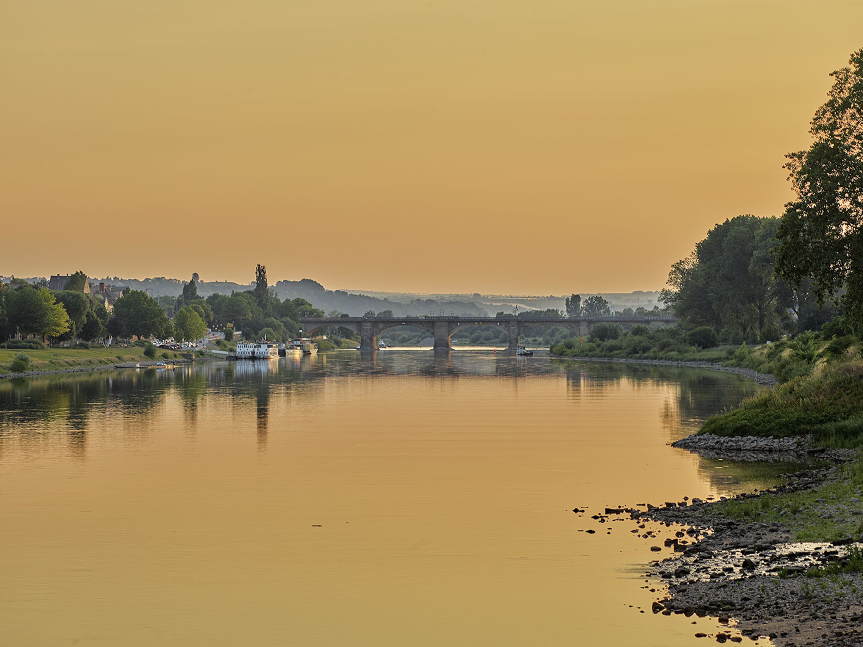 Ein Fluss mit einer Brücke, Booten und einer Stadtkulisse im Hintergrund.