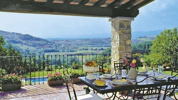 A covered outdoor dining area with a stone pillar, a table set for a meal, and a scenic view of rolling hills in the background. - Villa Stefano (Dicomano)