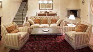 A living room with a striped sofa set, a coffee table, a patterned rug, a fireplace, and a staircase. - Villa Stefano (Dicomano)