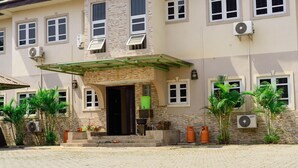 A multi-story building with a stone facade, multiple air conditioning units, and a covered entrance with steps leading to the door. - The Nook Apartments (Abuja)