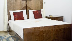 A bedroom with a wooden headboard, white bedding, and two red pillows. - The Nook Apartments (Abuja)