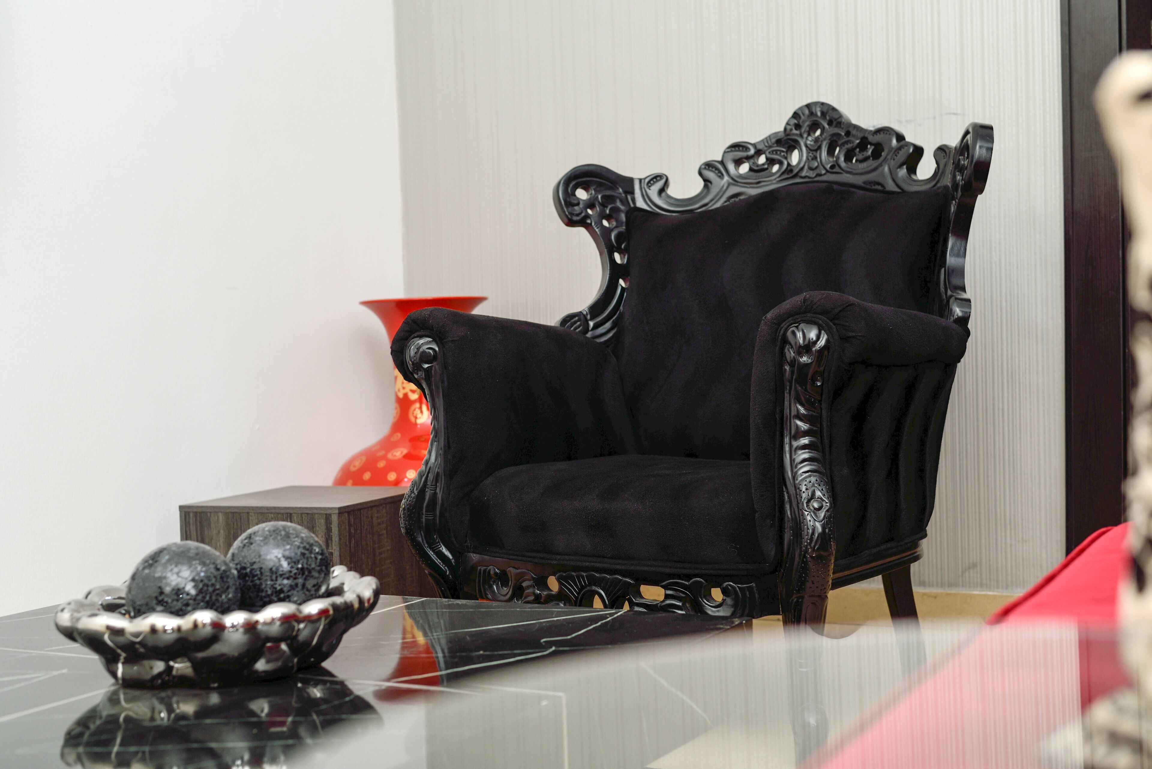 A black upholstered chair with ornate wooden carvings, positioned next to a small wooden table with a reflective surface.