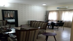 A hotel room with a dining area, a bed, a TV, and an air conditioning unit. - The Nook Apartments (Abuja)