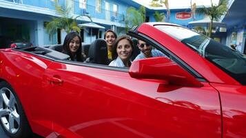 A red convertible with passengers, parked in front of a blue building with palm trees.