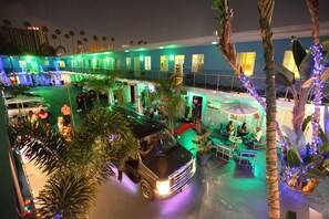 A hotel courtyard with a car, palm trees, and a dining area. - Banana Bungalow Hollywood Hotel & Hostel (Los Angeles)