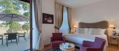 A hotel room with a bed, two armchairs, a small table, a window with curtains, and a view of the outdoors.