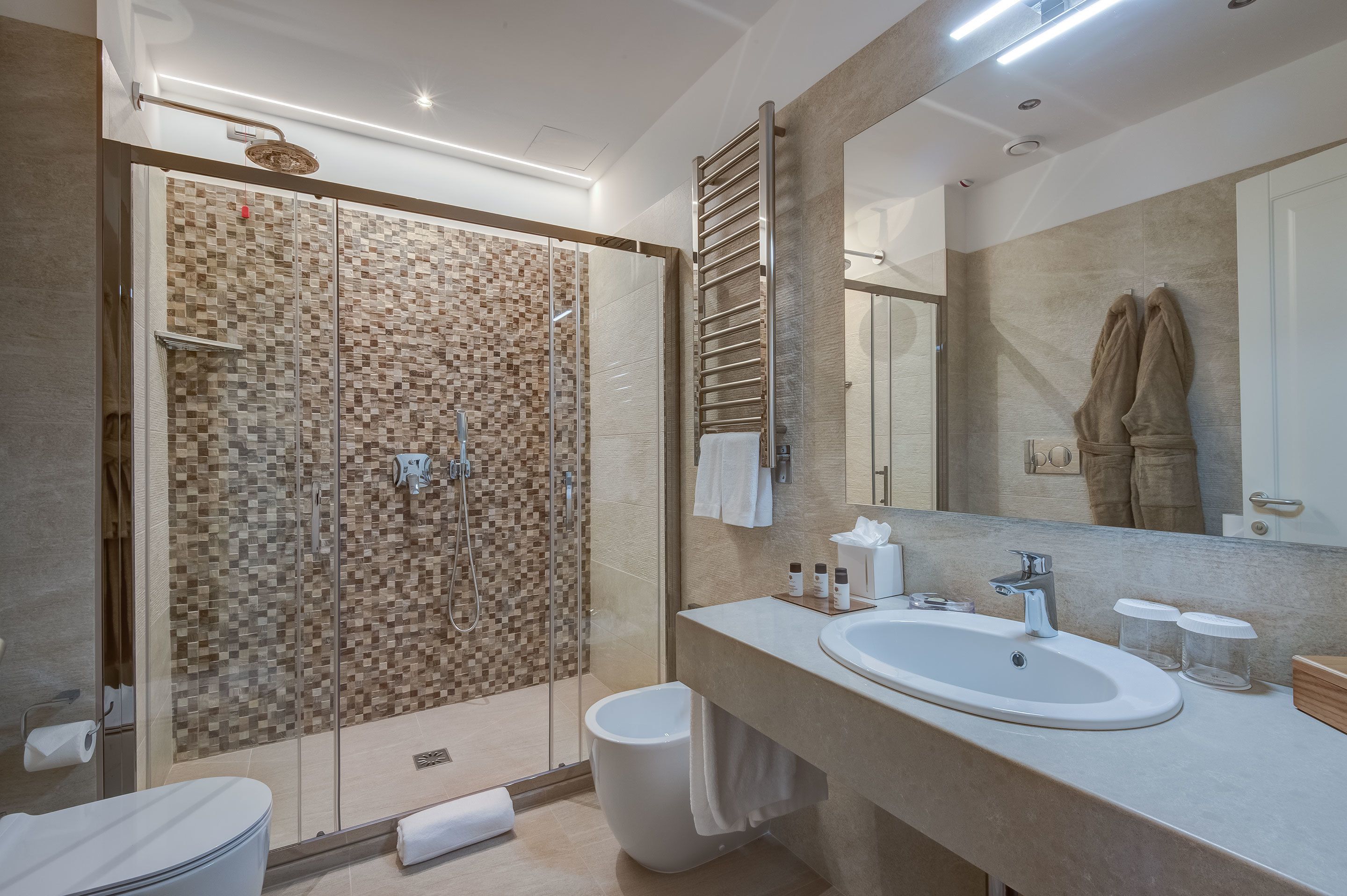 Une salle de bain moderne avec une douche à parois de verre, un grand miroir et un meuble-lavabo beige doté d’un évier et d’un porte-serviettes.