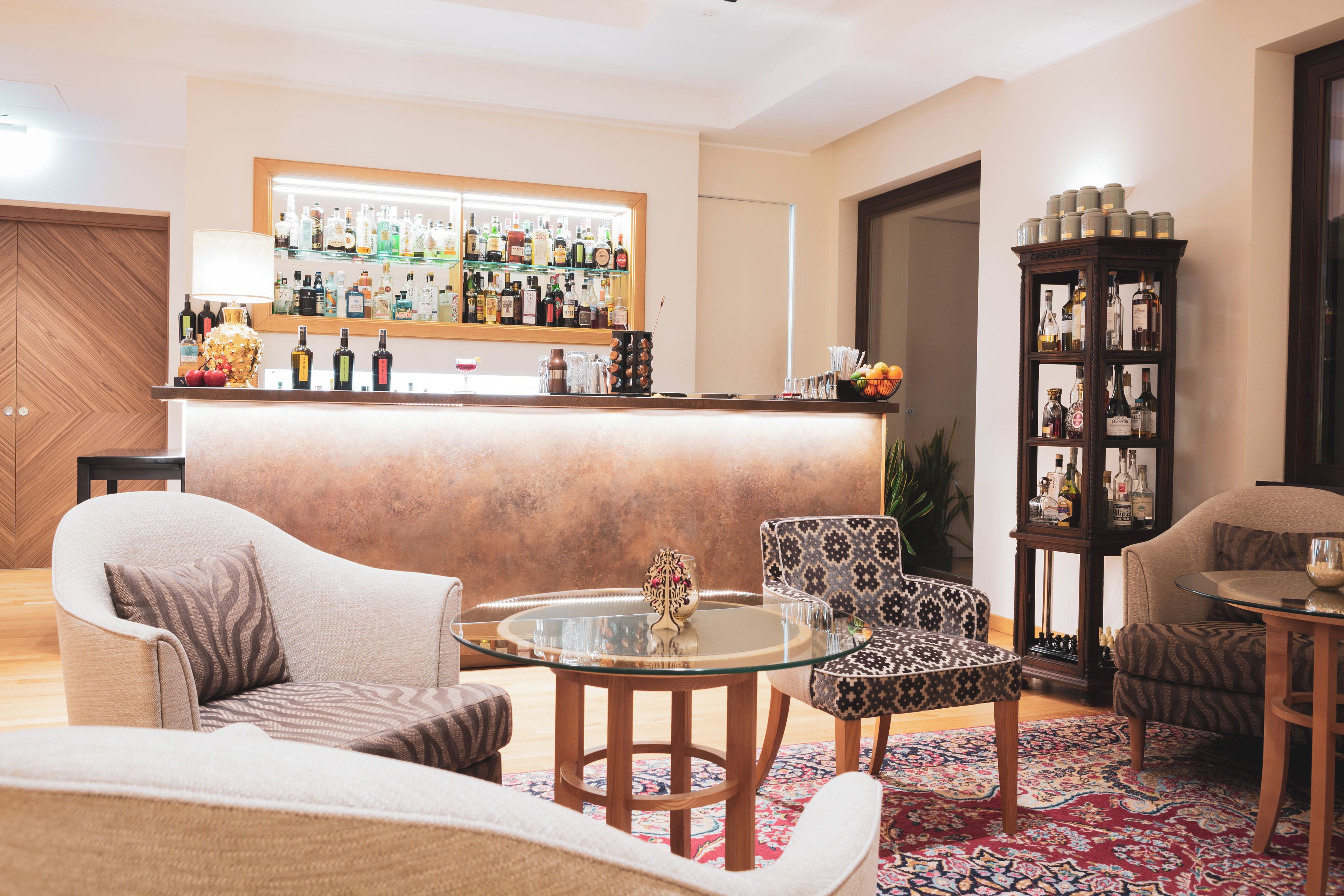 A bar area with a variety of bottles and glasses, a seating area with patterned chairs, and a decorative centerpiece on the table.