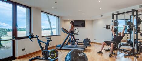 A gym with exercise equipment, large windows, and a view of the outdoors.
