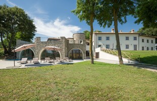 Un edificio con fachada de piedra, un amplio acceso en arco y un patio con césped y sillones de descanso.