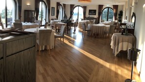 Un vaste espace dédié à la salle à manger, avec des tables rondes, des chaises élégantes et de grandes fenêtres offrant une vue sur l’extérieur.
