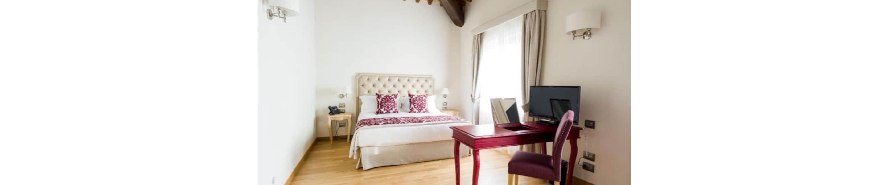 A bedroom with a bed, bedside table, lamp, TV, and a chair.