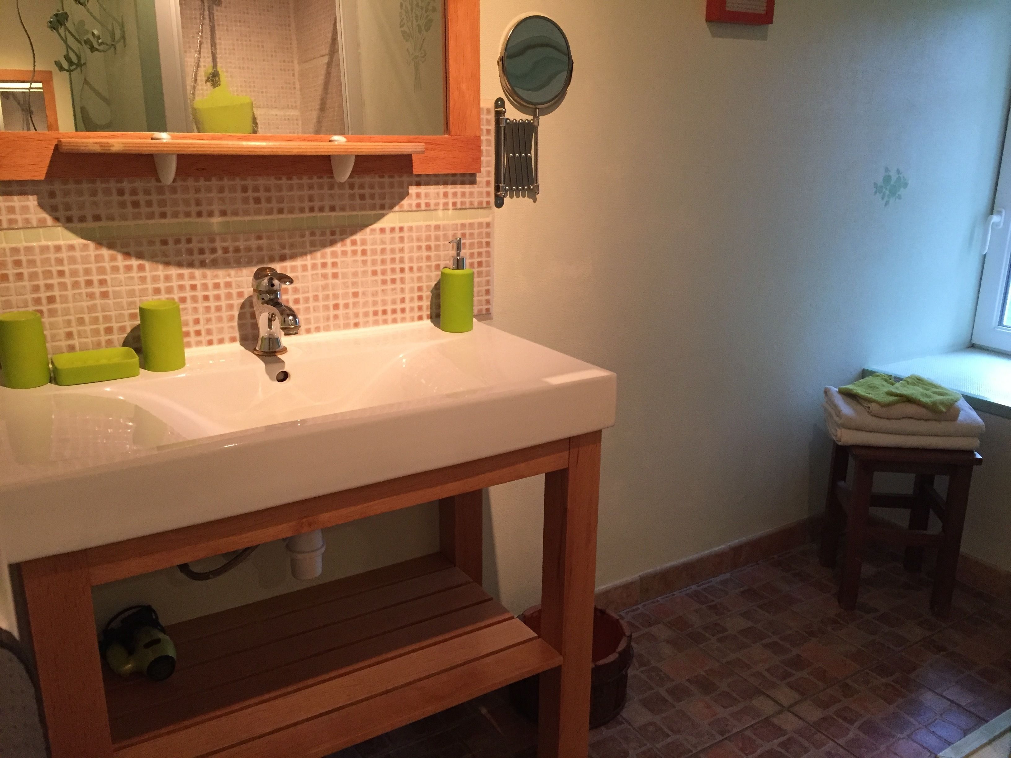 Une salle de bain avec un lavabo blanc, un savon vert et un tabouret en bois.