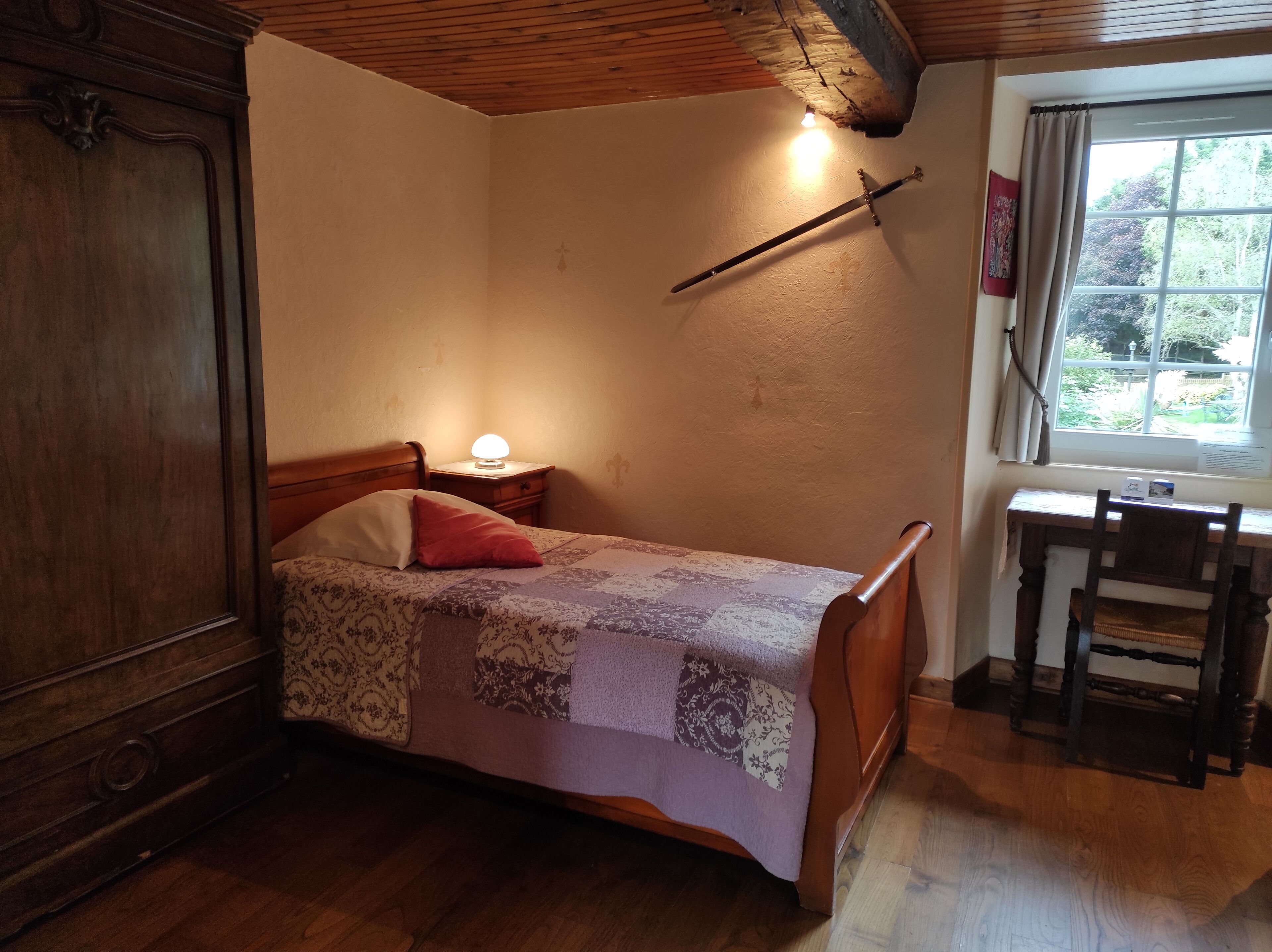 Une chambre à coucher avec un lit en bois, une table de chevet avec une lampe, un bureau en bois avec une chaise et une fenêtre avec des rideaux.