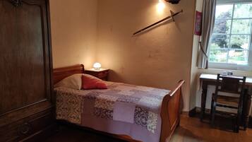 Une chambre à coucher avec un lit en bois, une table de chevet avec une lampe, un bureau en bois avec une chaise et une fenêtre avec des rideaux.