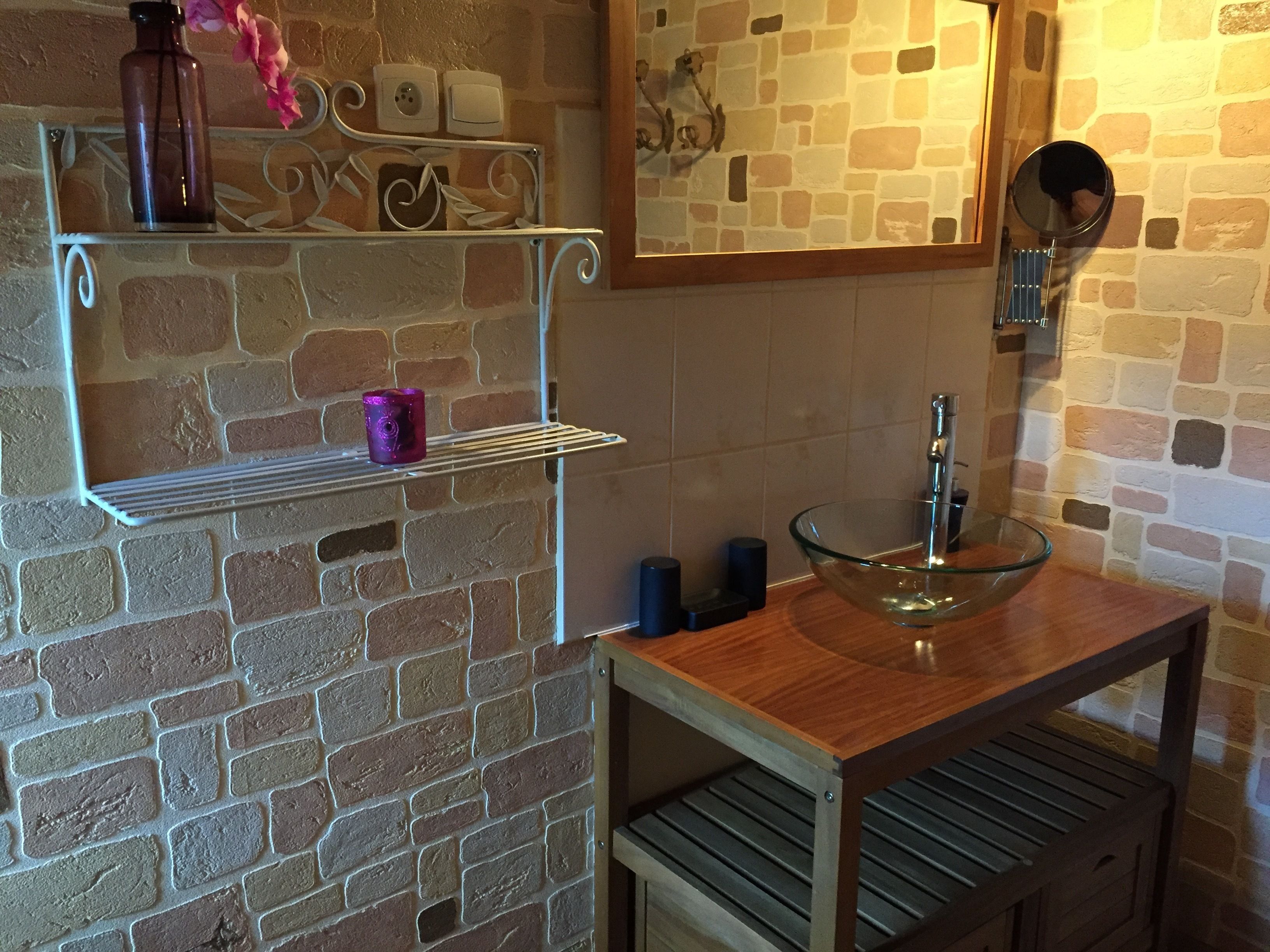 Une salle de bain avec un mur en briques, un meuble-lavabo en bois, un lavabo en verre et un miroir.