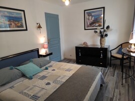 Un dormitorio con cama, mesita de noche, cómoda, una silla y dos cuadros en las paredes.