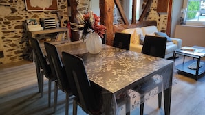 A rustic dining area with a stone wall, wooden beams, and a table with chairs. - Au Clos du Lit - Chambres d'hôtes (Lamballe-Armor)