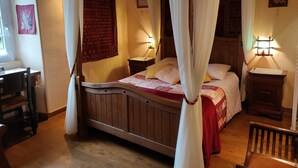 A traditional wooden bed with a canopy, a bedside table with a lamp, and a wall with a religious painting. - Au Clos du Lit - Chambres d'hôtes (Lamballe-Armor)