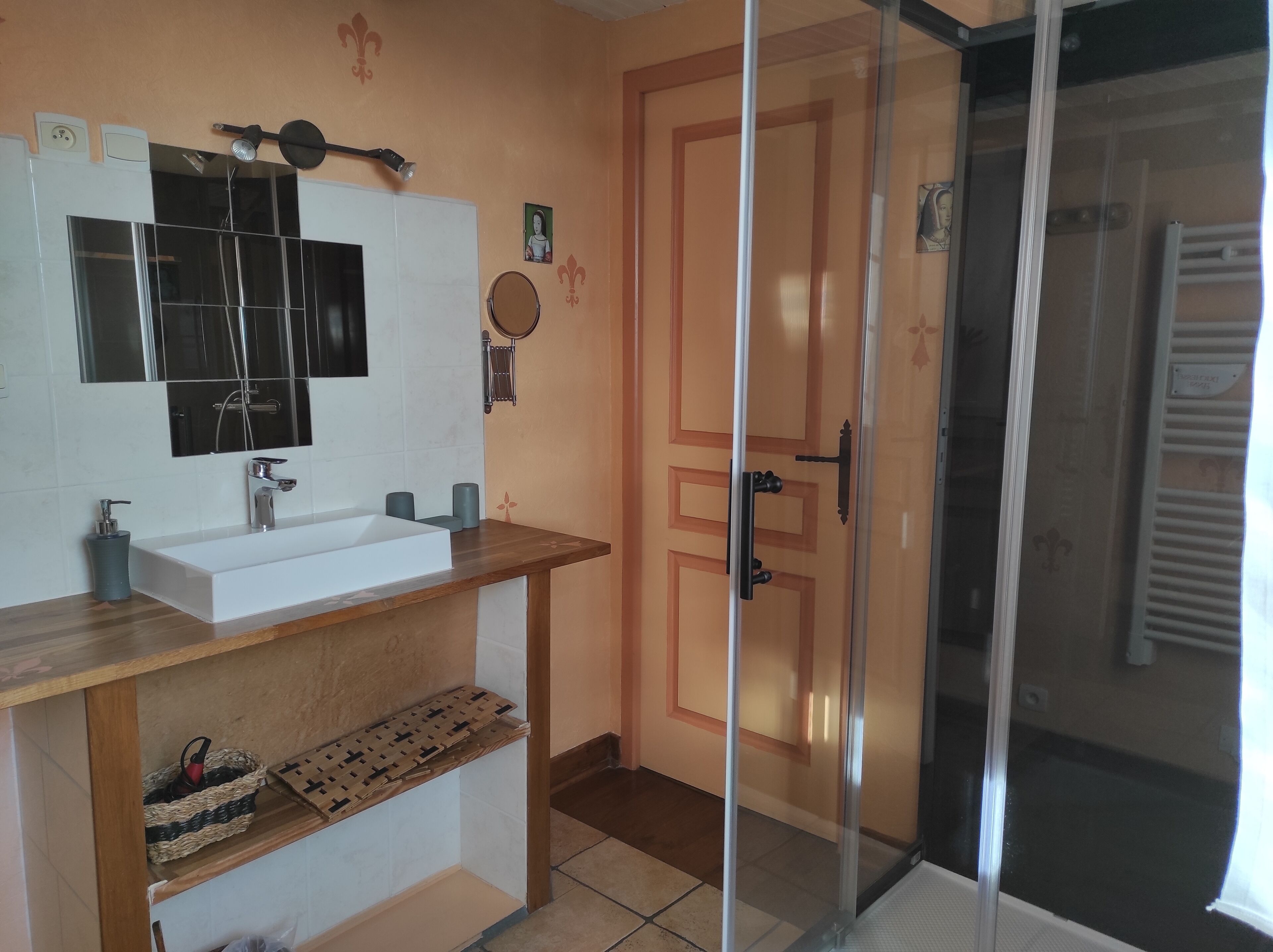 Ein Badezimmer mit einem weißen Waschbecken, einem Spiegel und einer Holzkommode. Eine Duschabtür aus Glas und ein Handtuchhalter sind an der Wand angebracht.