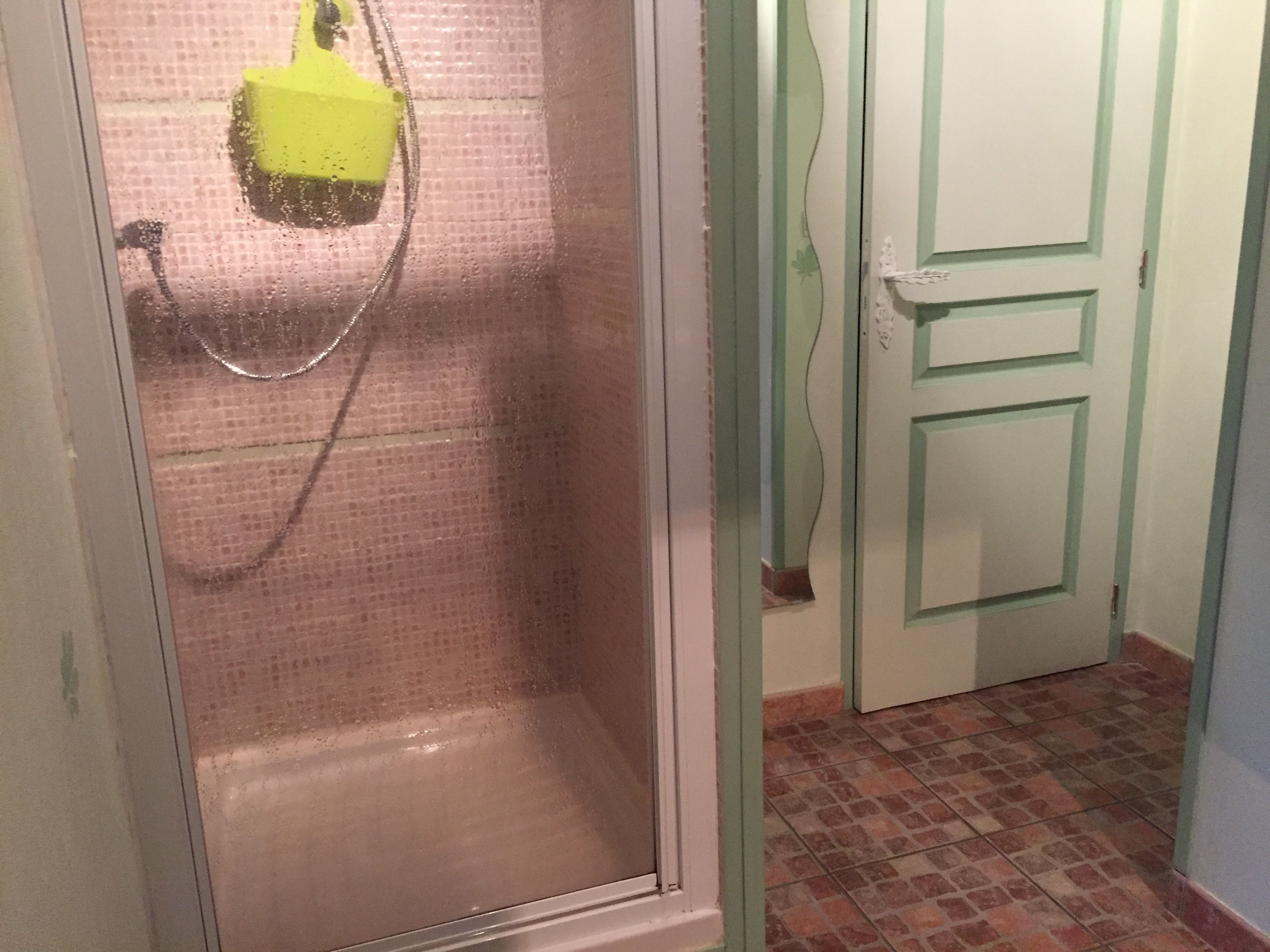 Un baño con ducha, piso de baldosas y una puerta con picaporte decorativo.