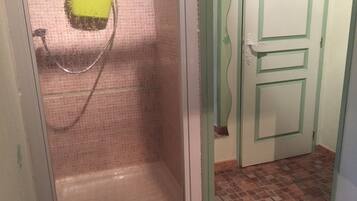 Un baño con ducha, piso de baldosas y una puerta con picaporte decorativo.
