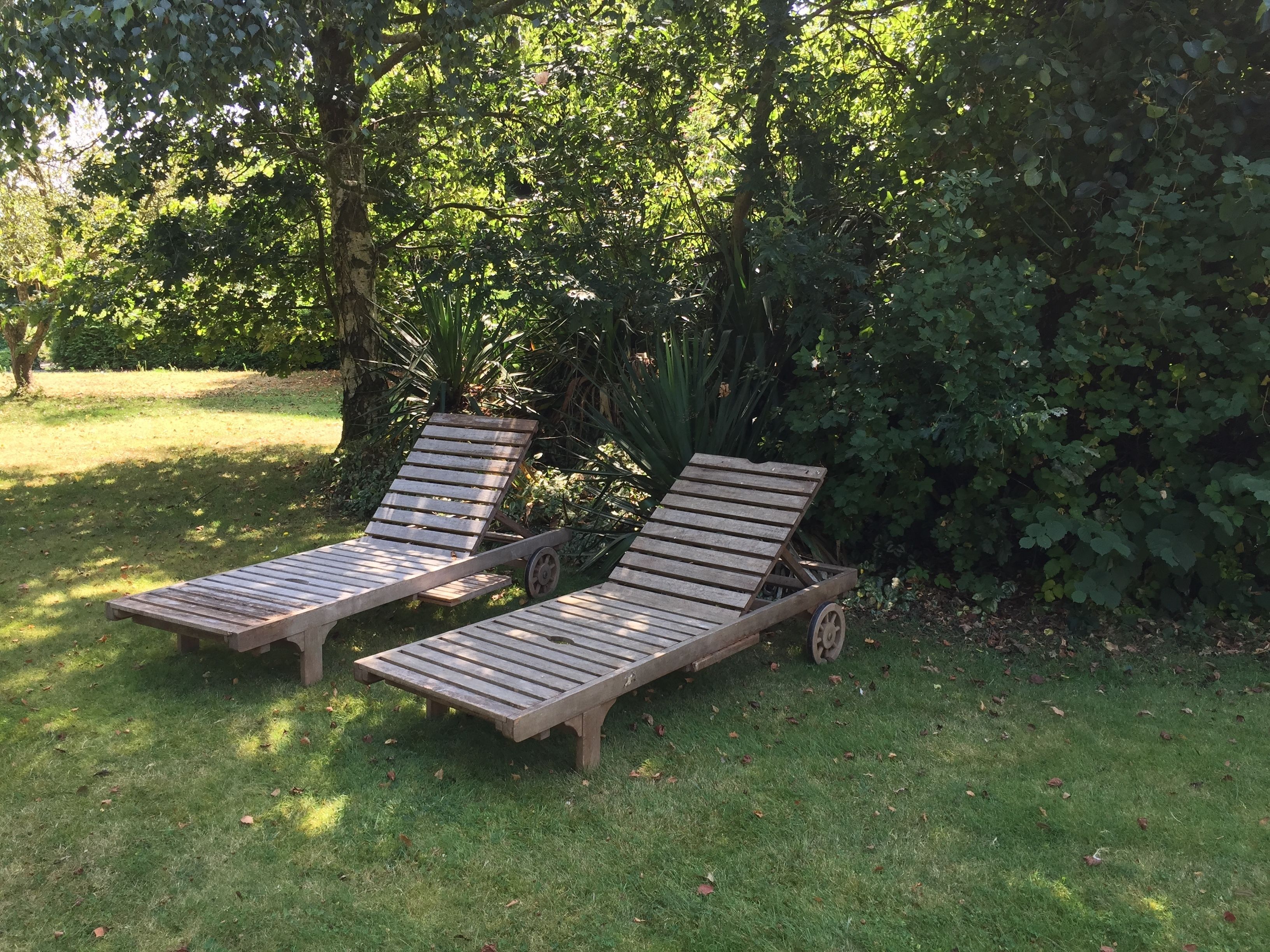 Two wooden lounge chairs with wheels, positioned on a grassy lawn with dense foliage in the background.