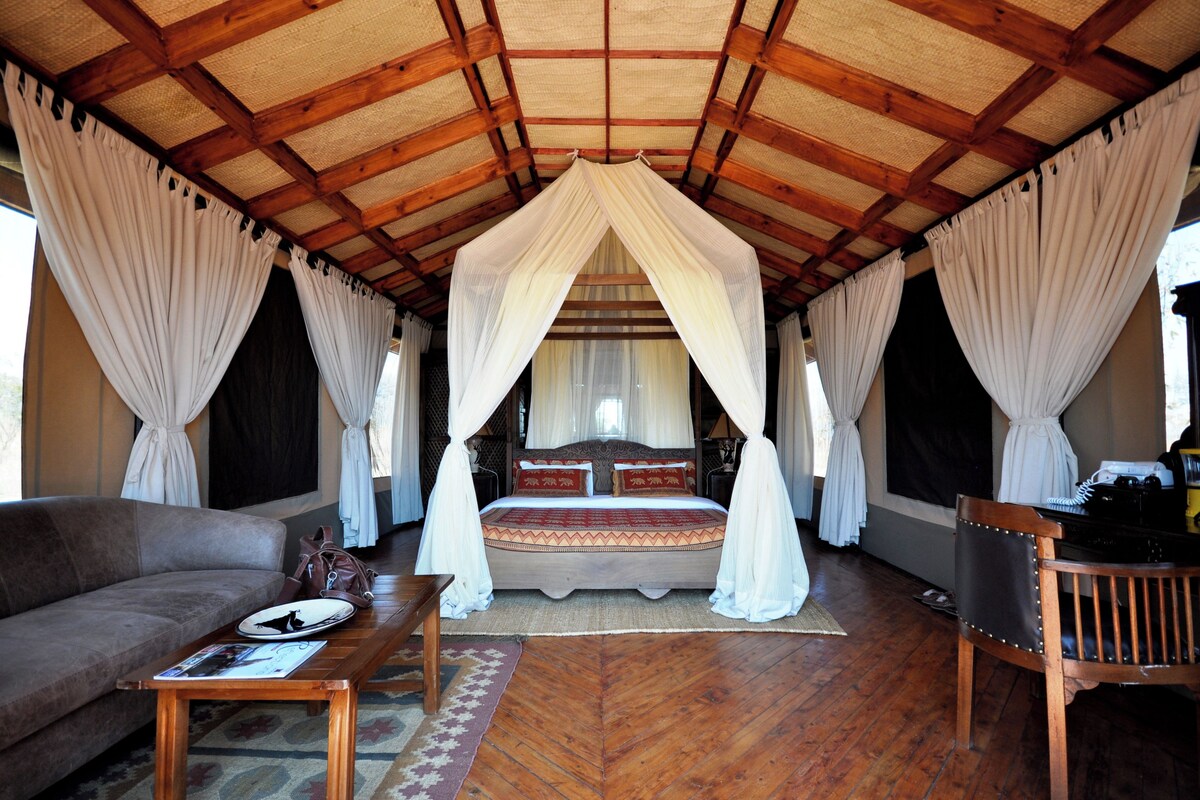 A bedroom with a canopy bed, wooden furniture, and a herringbone-patterned floor.