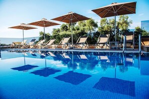 A poolside area with lounge chairs and umbrellas, a clear blue pool, and trees in the background. - Panorama Exclusive Suites (Parga)
