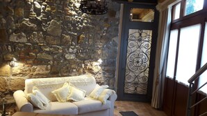 Une pièce chaleureuse avec un mur en pierre, un canapé blanc agrémenté de coussins à motifs et une porte décorative en métal.