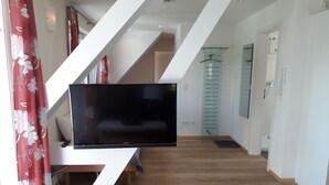 Un salon moderne avec un téléviseur à écran plat posé sur un meuble blanc, un plancher en bois et un escalier avec des rampes blanches.