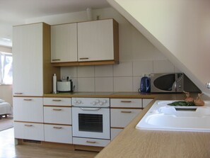 Cuina amb armaris blancs, forn de pared, microones i una barra.