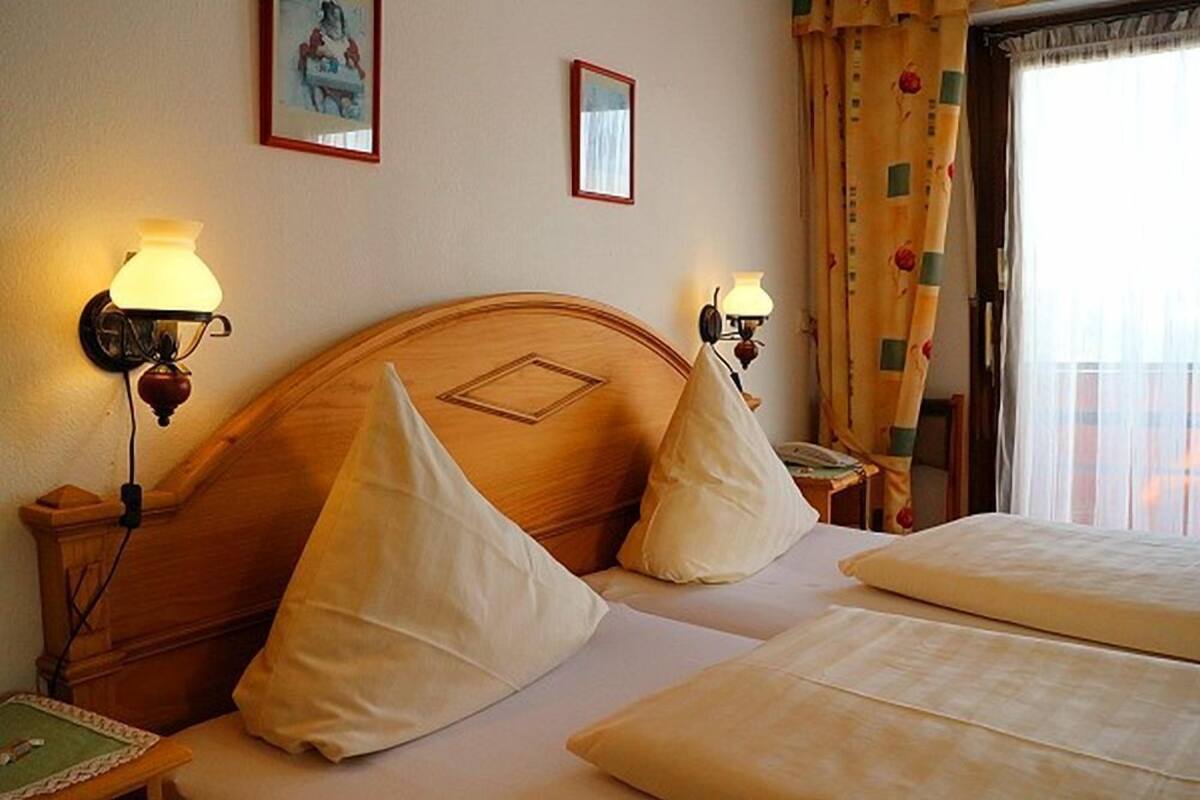 A hotel room with two beds, a wooden headboard, bedside lamps, and a small table with a lamp.