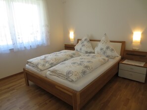 A double bed with rose-patterned bedding, wooden headboard, bedside tables with wall-mounted lamps, and a wooden floor. - Buche (Ueberlingen)