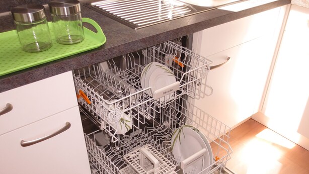 A kitchen with a dishwasher, a sink, and a green cutting board.