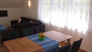 A dining area with a wooden table, blue tablecloth, and chairs. A bowl of fruit is on the table.