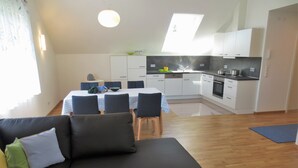 A modern kitchen with white cabinets, a dining area with a table and chairs, and a black sofa with cushions.