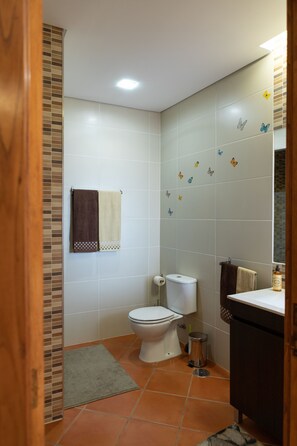 Un baño con inodoro, lavamanos y espejo. Hay dos toallas colgadas en la pared.