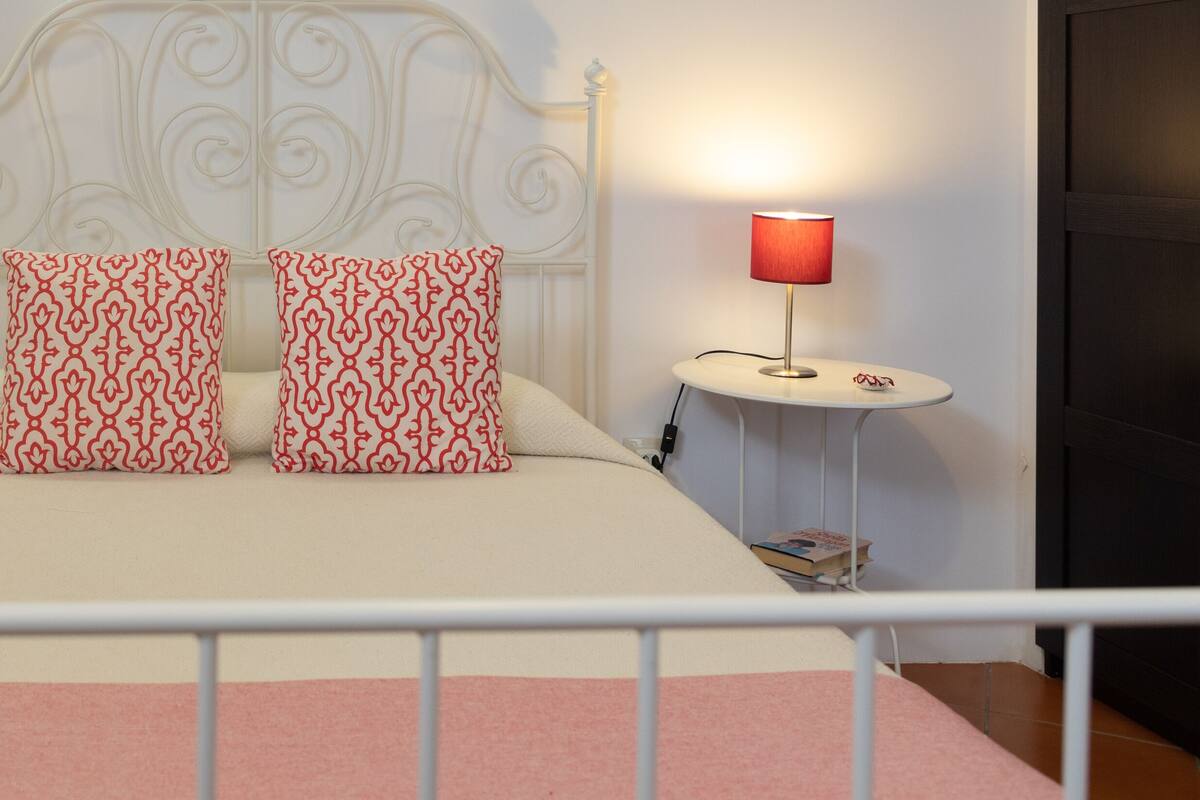 A neatly made bed with two patterned pillows, two bedside tables with lamps, and a white metal headboard.