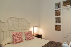 Una cama bien tendida con almohadas estampadas, una lámpara de noche y una mesita de noche con un libro y un florero.