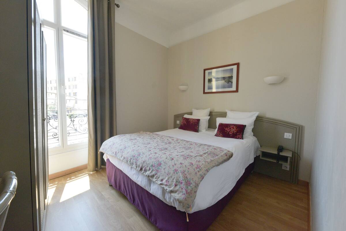 A bedroom with a bed, a nightstand, a window with curtains, and a wall-mounted picture.