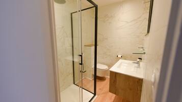 A modern bathroom with a glass-enclosed shower, a wooden vanity, and a marble-tiled wall.