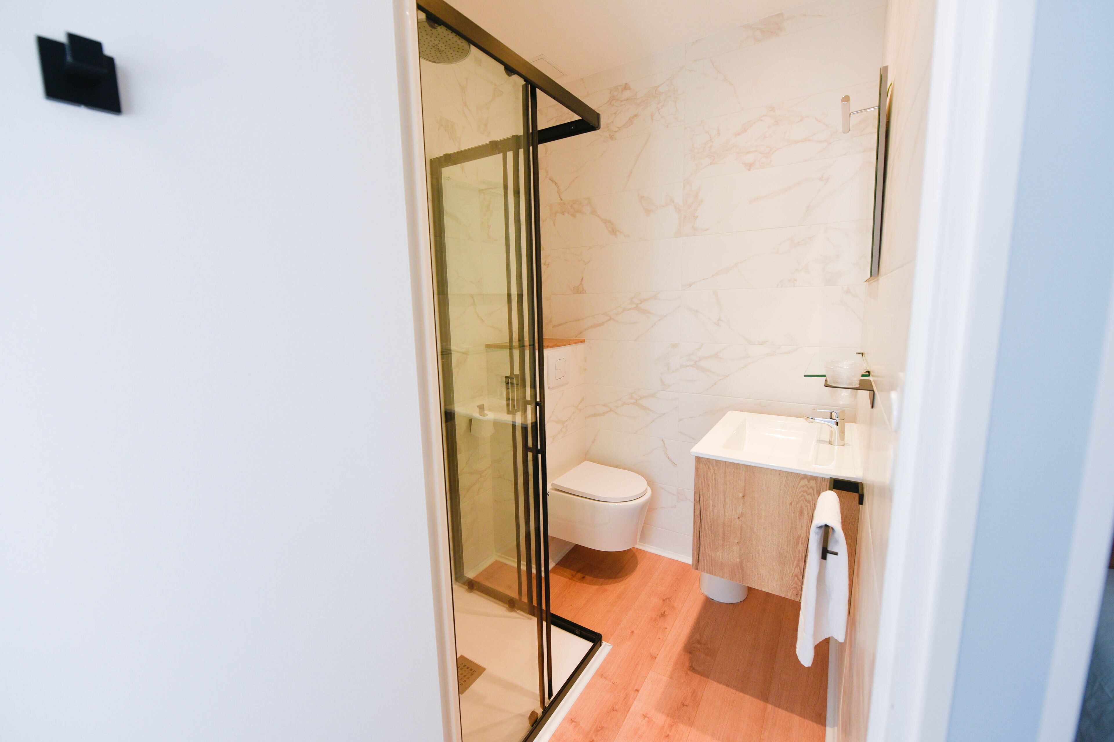A modern bathroom with a glass shower enclosure, a white toilet, and a wooden vanity.
