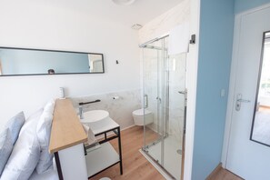 Um banheiro moderno com box de vidro, pia branca e painel de fundo de mármore.