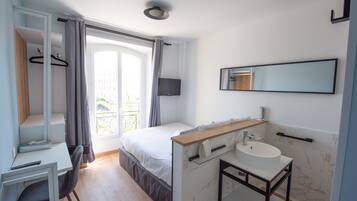 A modern bedroom with a bed, a desk, a bathroom with a sink and mirror, and a balcony view.