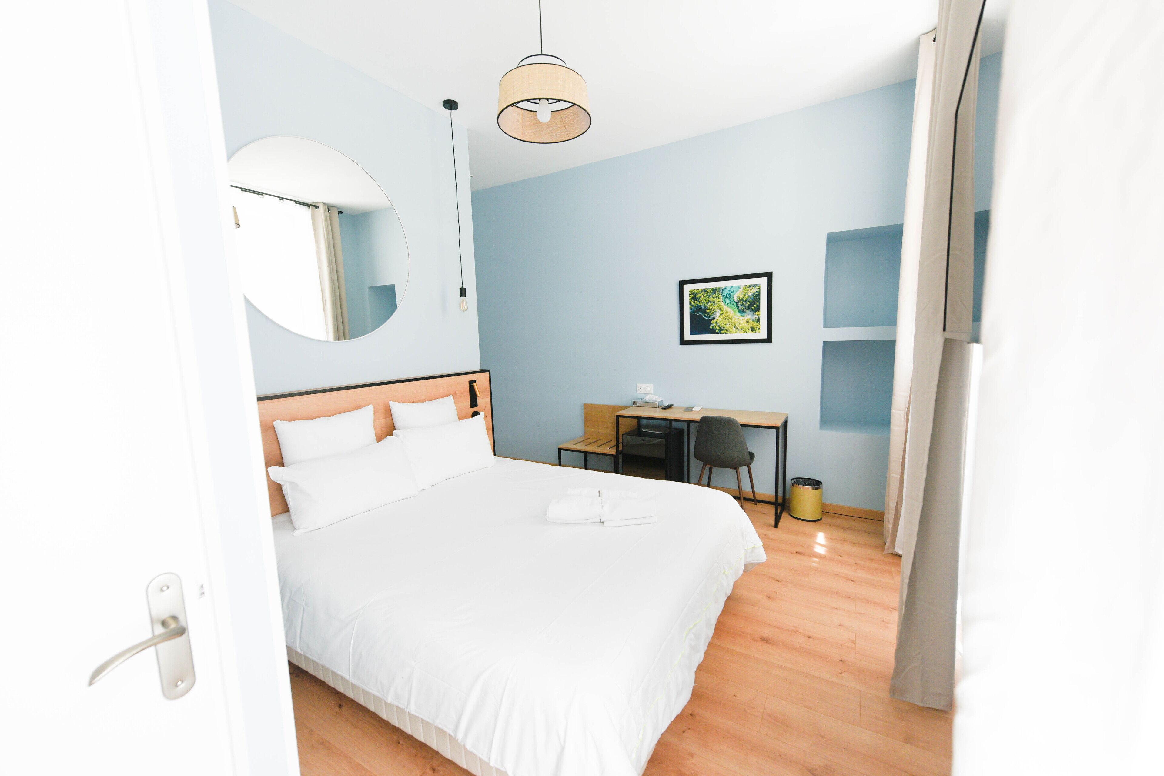 A hotel room with a bed, a desk, a chair, a mirror, and a picture on the wall.